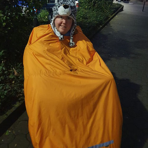 Eine SMA-Patientin sitzt draußen im Rollstuhl und lächelt in die Kamera. Sie trägt Winterkleidung: eine warme Mütze sowie eine spezielle Daunenjacke für Rollstuhlfahrer.