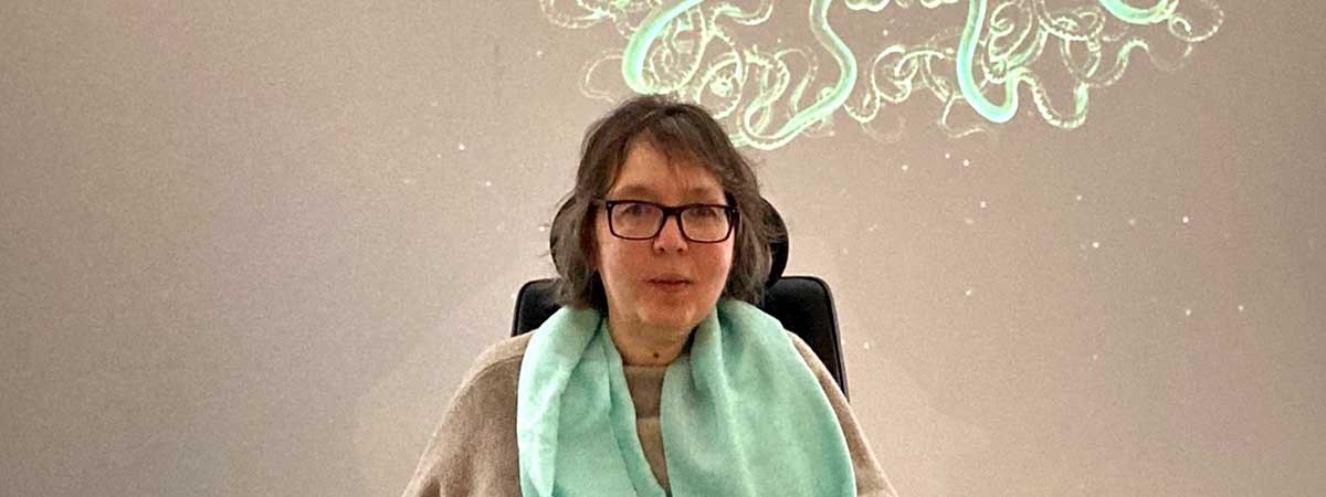SMA-Betroffene Camilla sitzt in ihrem Elektrorollstuhl in einer Ausstellung vor einer grünen Illumination an einer weißen Wand.