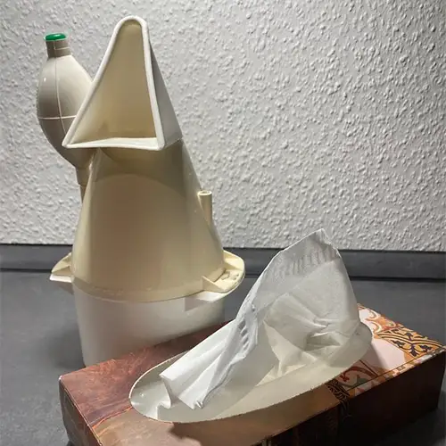 Ein Inhalator und eine Box mit Taschentüchern auf einer dunklen Oberfläche vor einer weißen Wand.