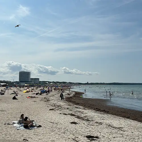 Ein Foto vom Strand in Warnemünde: Einige Menschen sonnen sich im Sand, während andere im Meer schwimmen.