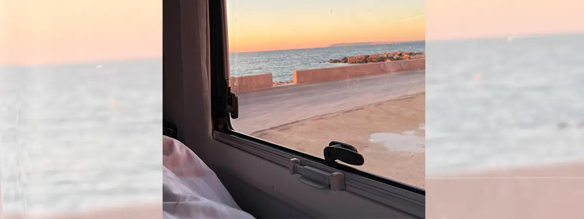 Ein Foto, das den Blick aus dem Wohnmobil auf einen Sonnenaufgang am Meer zeigt.