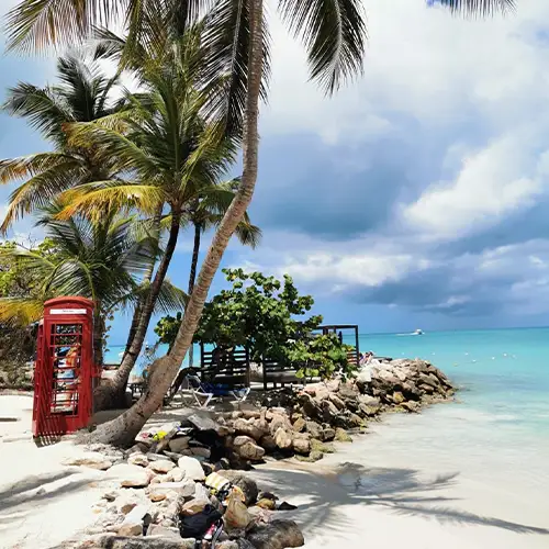 Ein weißer Sandstrand mit türkisem Meer und Palmen sowie einer roten Telefonzelle.