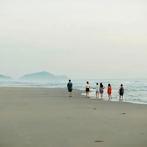 Eine Gruppe junger Menschen spaziert am Strand entlang und genießt den Blick aufs Meer.