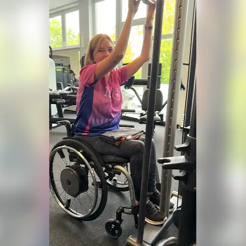Ein Foto von Svenja, die eine Übung im Fitnessstudio ausführt und in die Kamera lächelt.