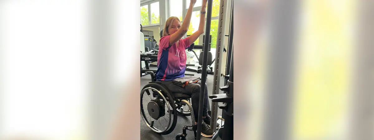 Ein Foto von Svenja, die eine Übung im Fitnessstudio ausführt und in die Kamera lächelt.