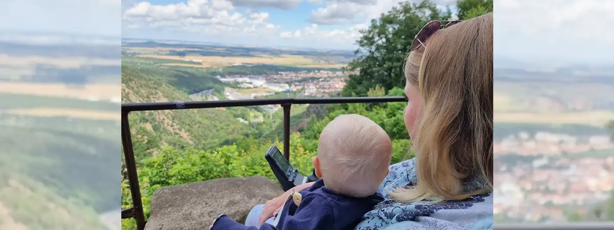 Sandra sitzt im E-Rolli mit Baby auf dem Schoß auf einem Hügel und schaut in die Ferne