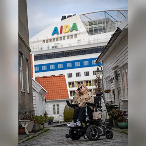 Ein Foto von Lilli im Elektrorollstuhl, während hinter ihr ein AIDA-Kreuzfahrtschiff ist.