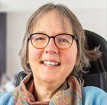 Portrait-Foto der 49-jährigen SMA-Patientin Camilla. Das Redaktionsmitglied sitzt im Rollstuhl und lächelt in die Kamera.